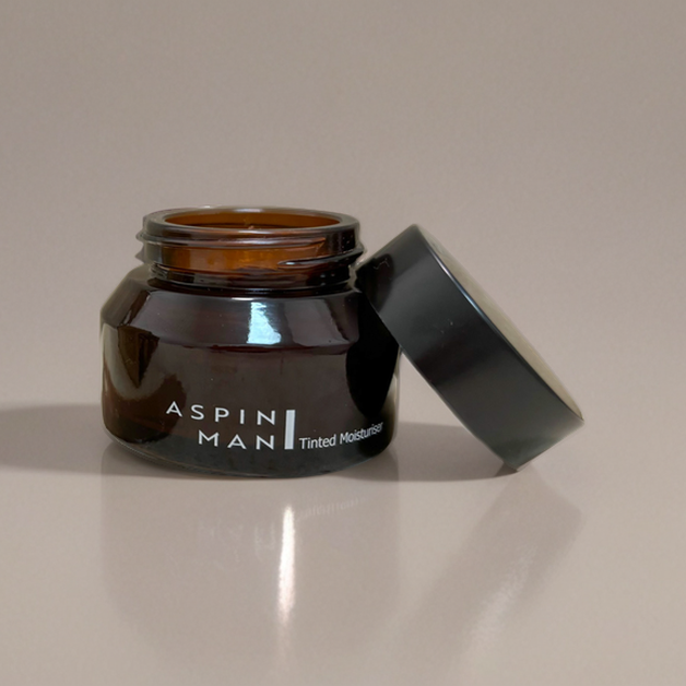 Aspin Man Tinted Moisturiser with the lid off, showing the amber-coloured glass jar on a taupe background.